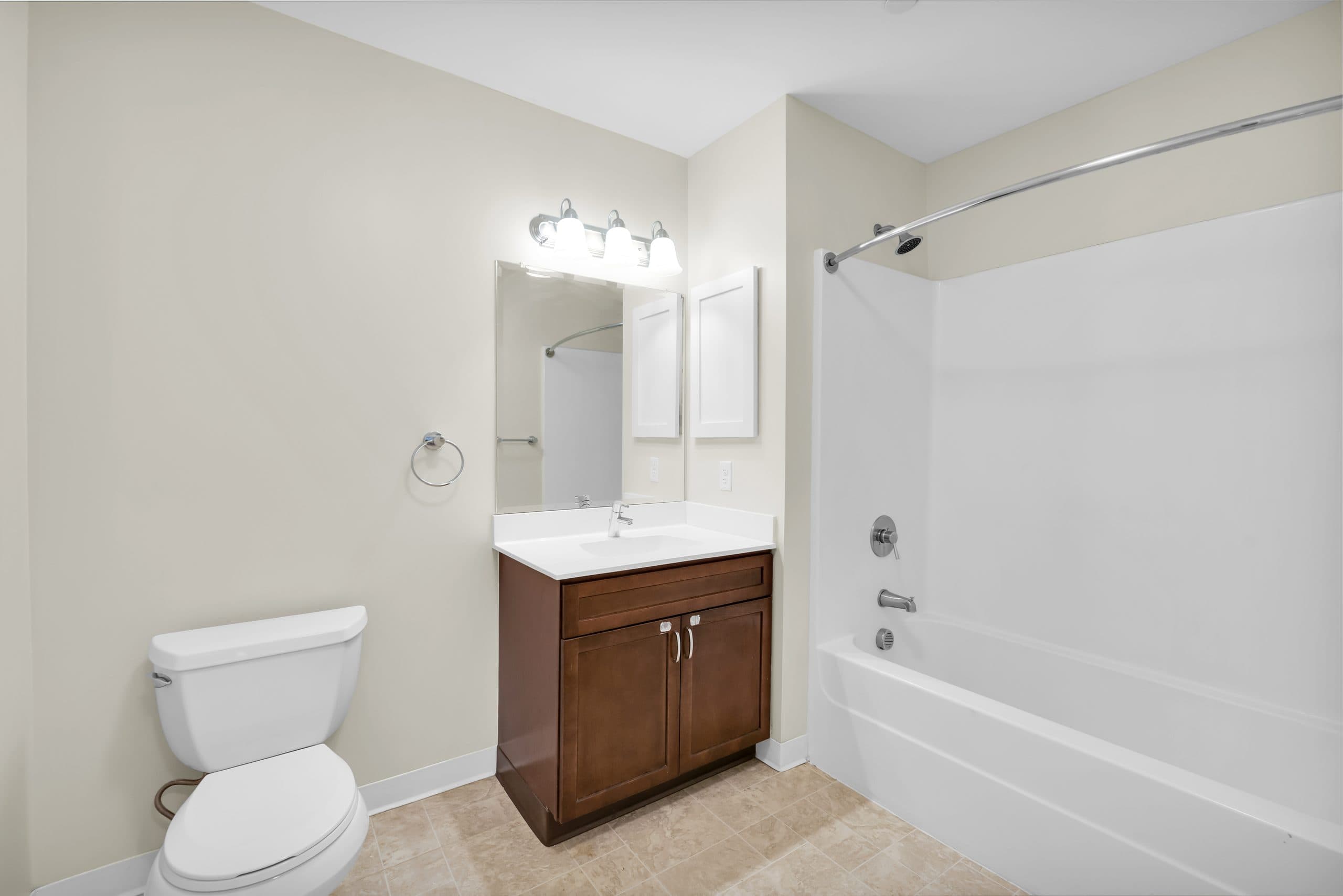 A bathroom with a tub and shower, a wood vanity and a lit mirror