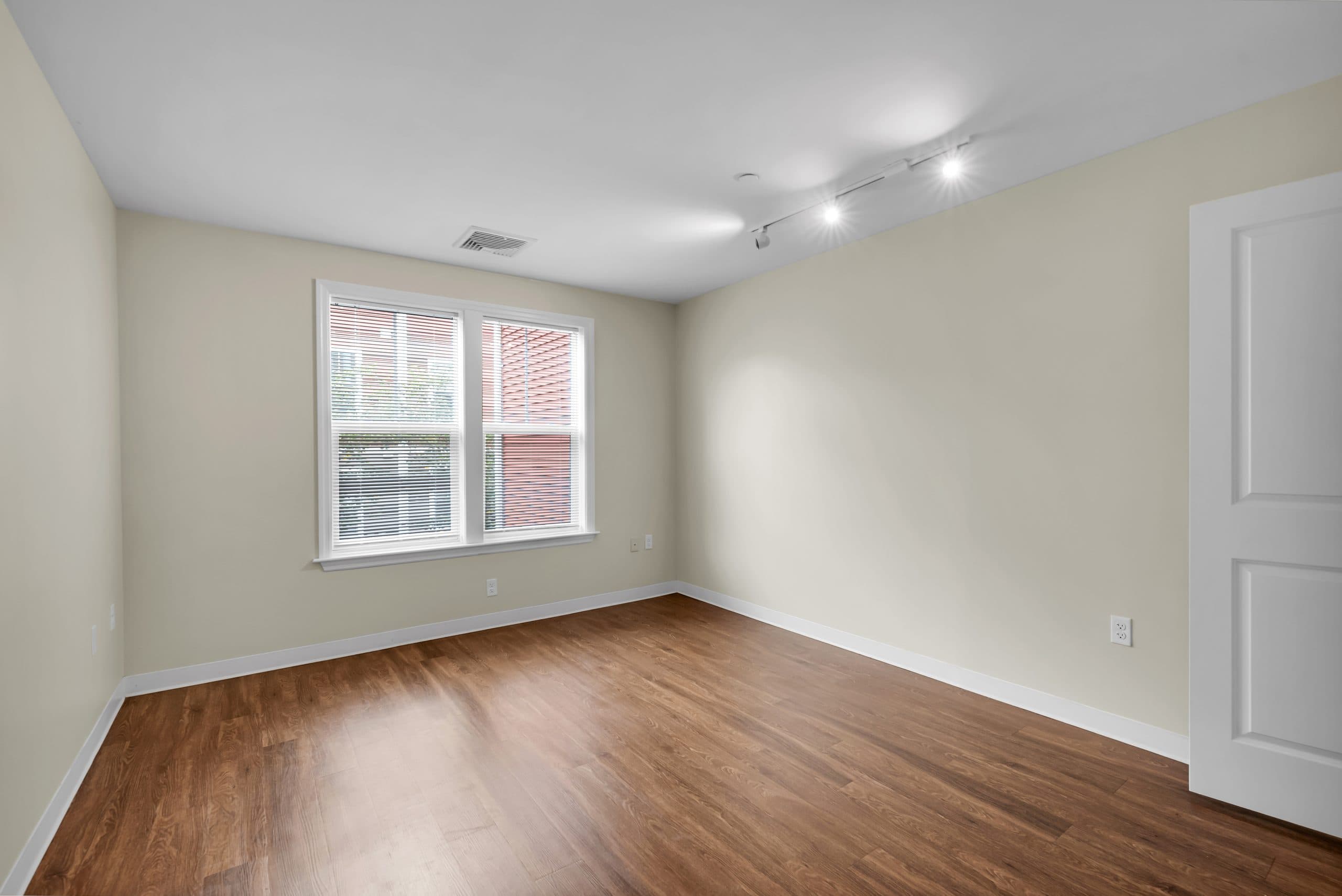 A bedroom with plank flooring, a wide window and track lighting