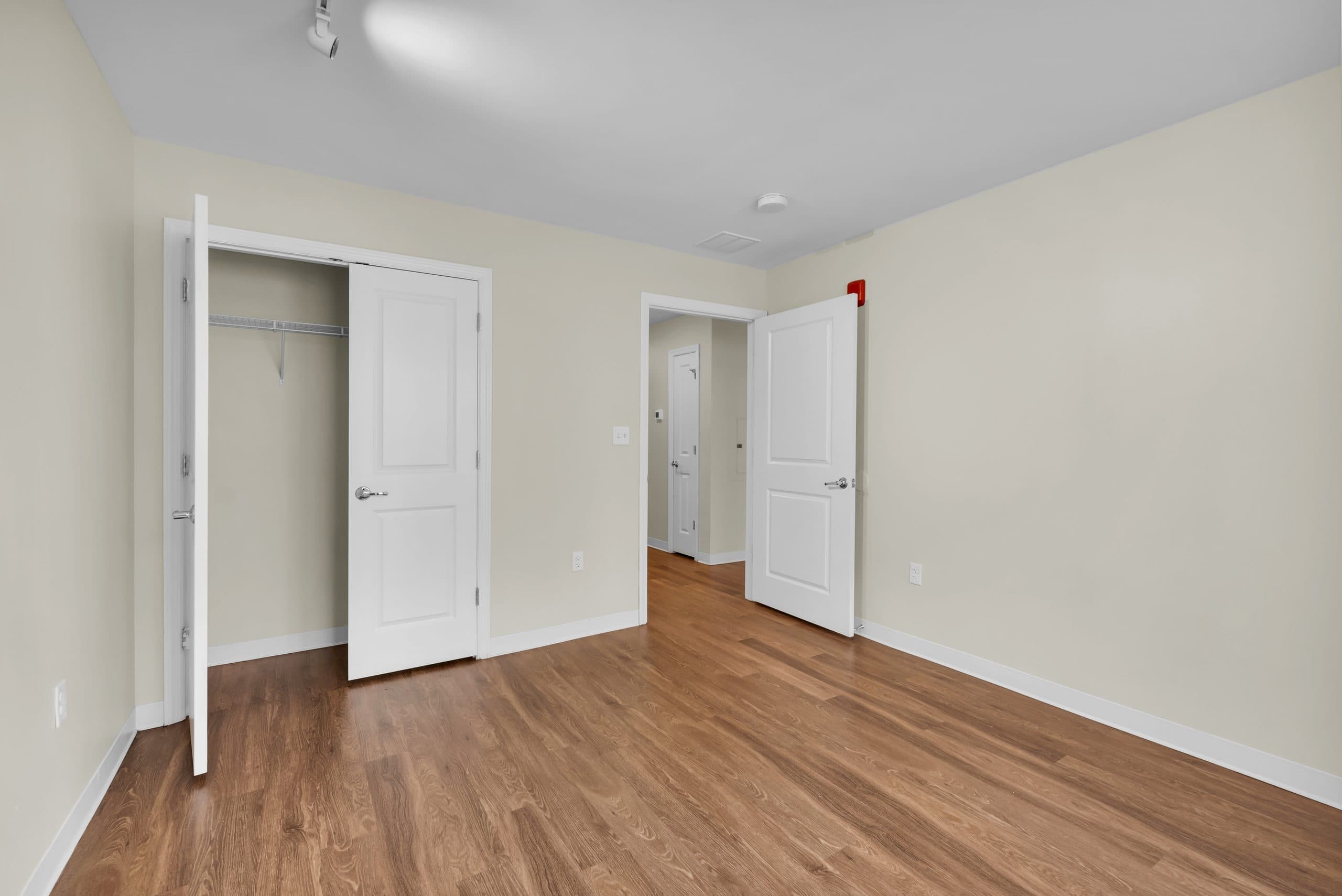 A bedroom with its closet doors open and a doorway through to the hall