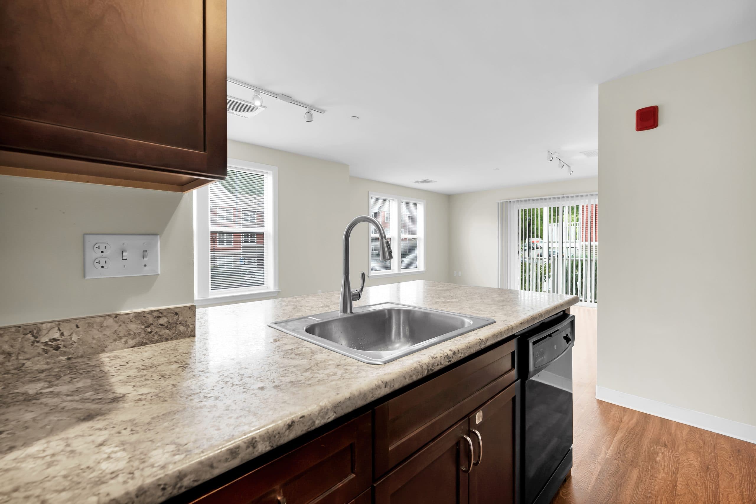 A kitchen with wood cabinets, a granite-look counter with a sink, black appliances and windows beyond