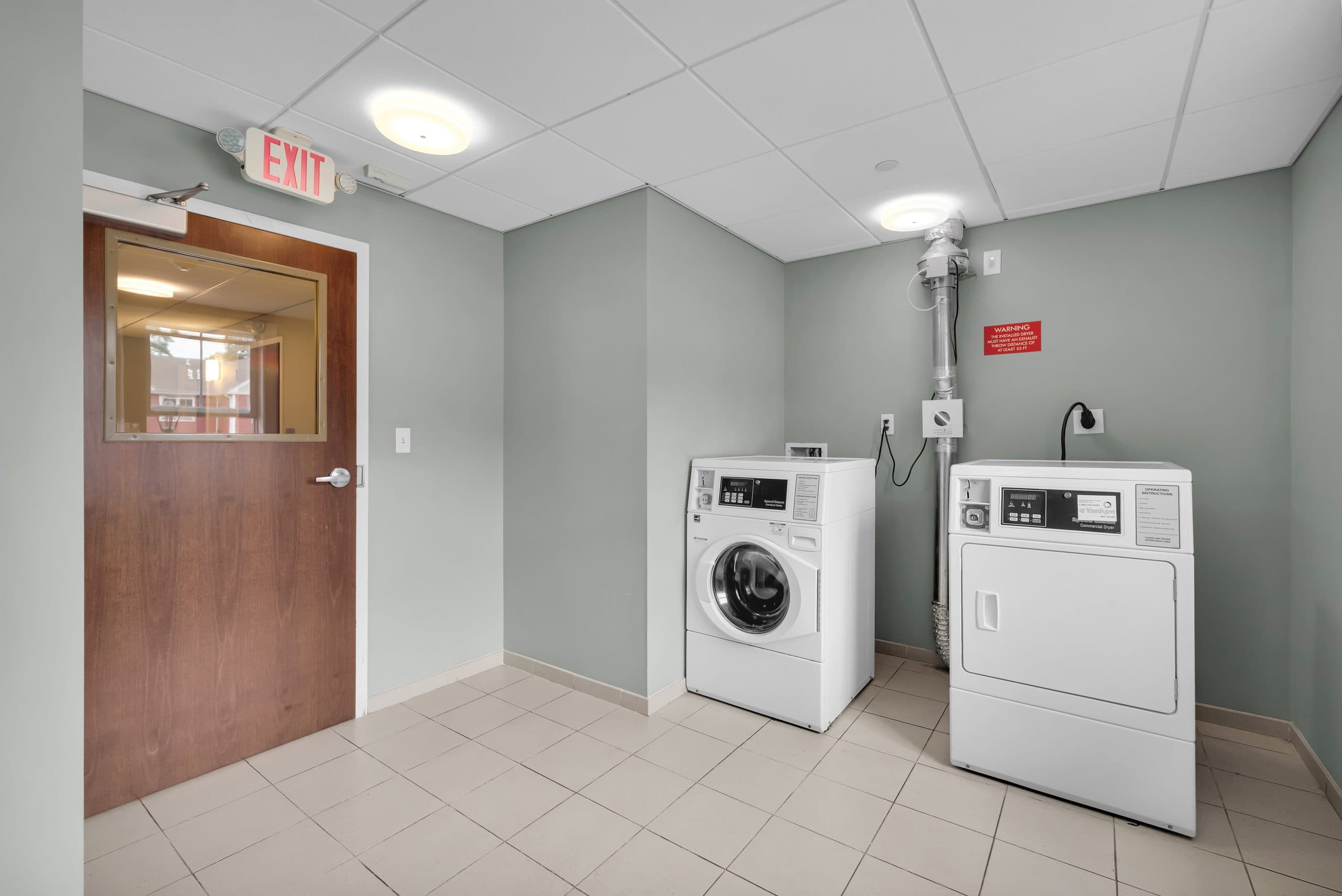 A building laundry room with a washer and dryer and tiled floor
