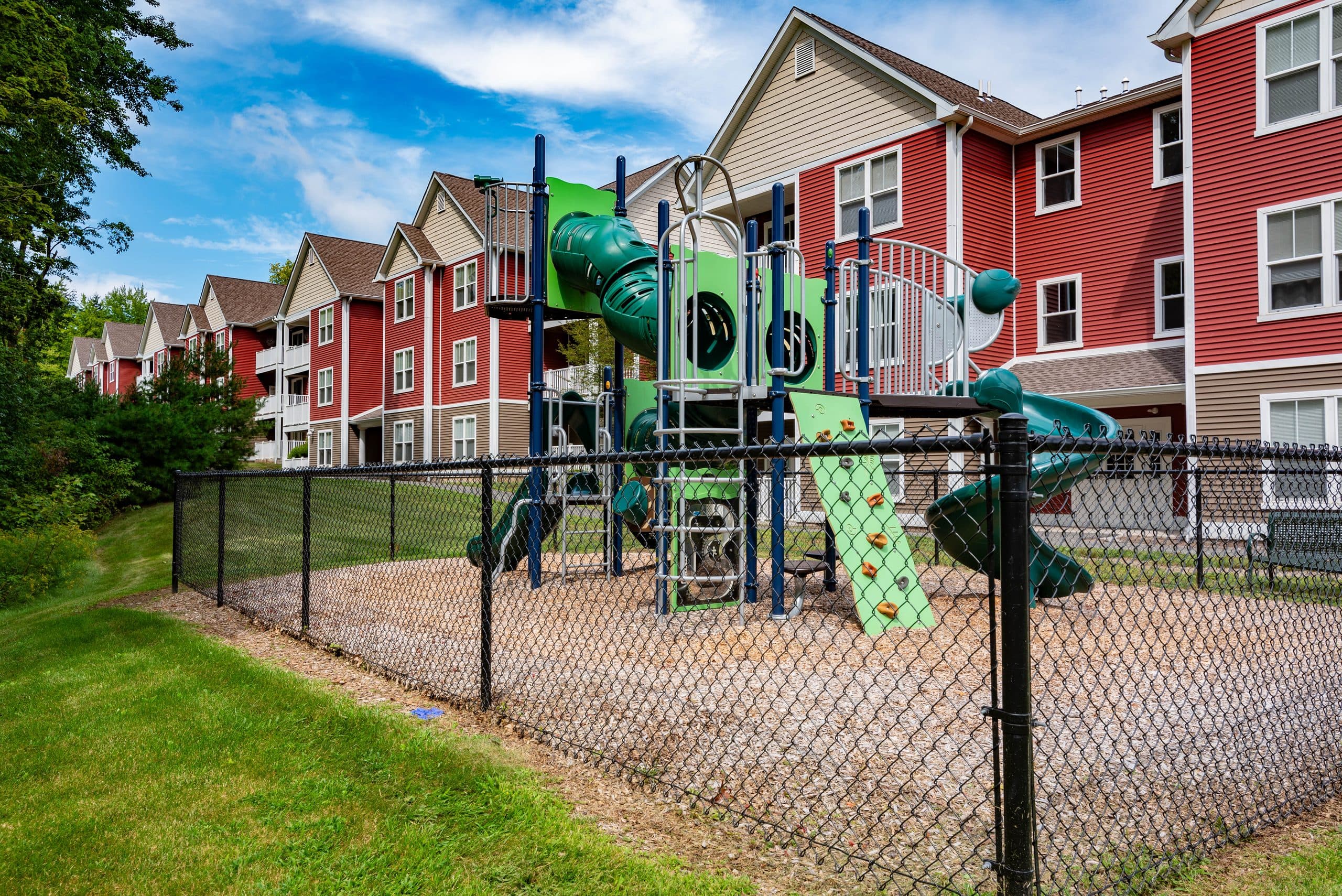Fenced playground with green climbing equipment and slides beside the Brook Hill Village buildings
